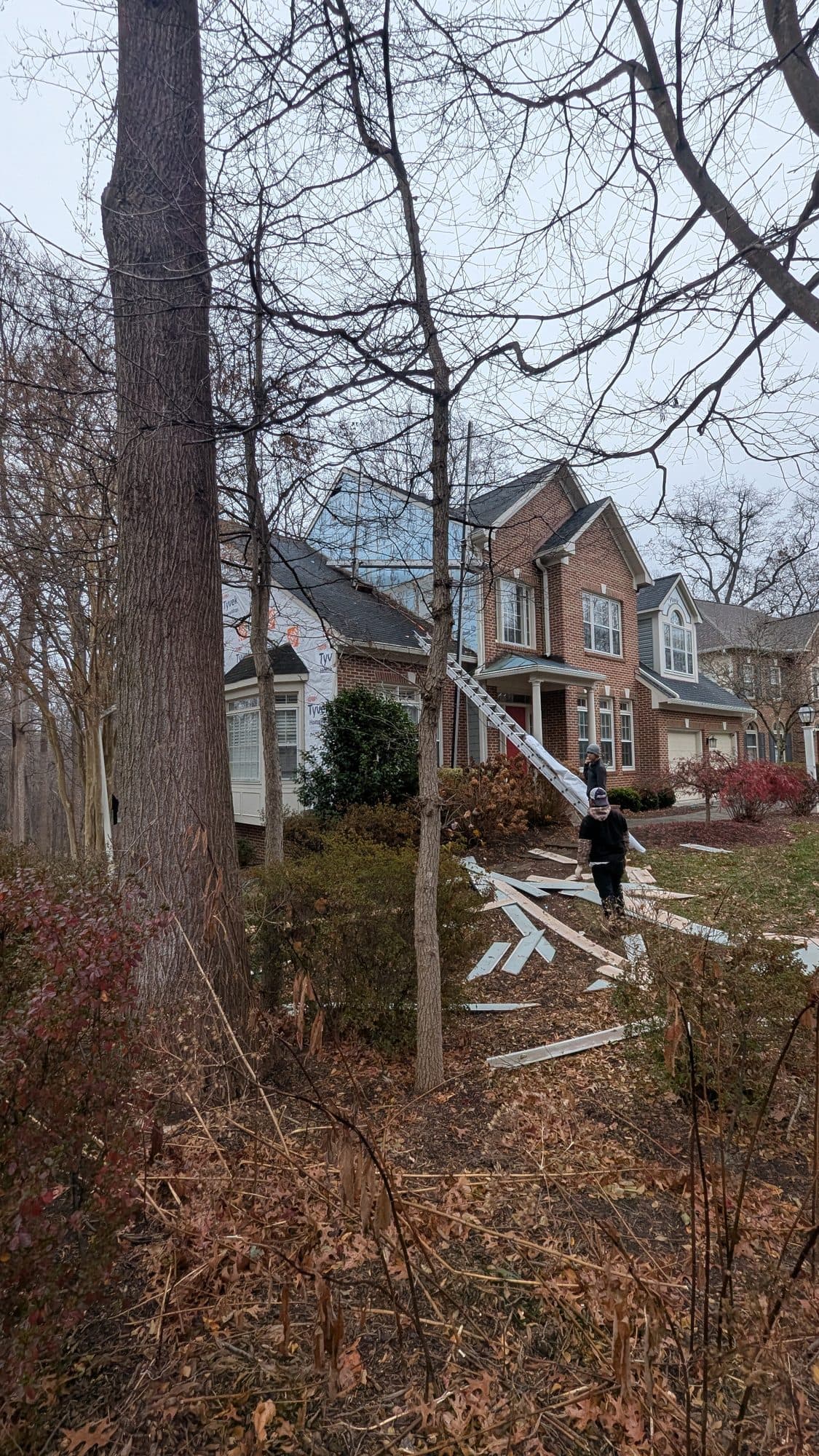 House mid-siding-replacement with materials staged on the ground and crew working from a ladder