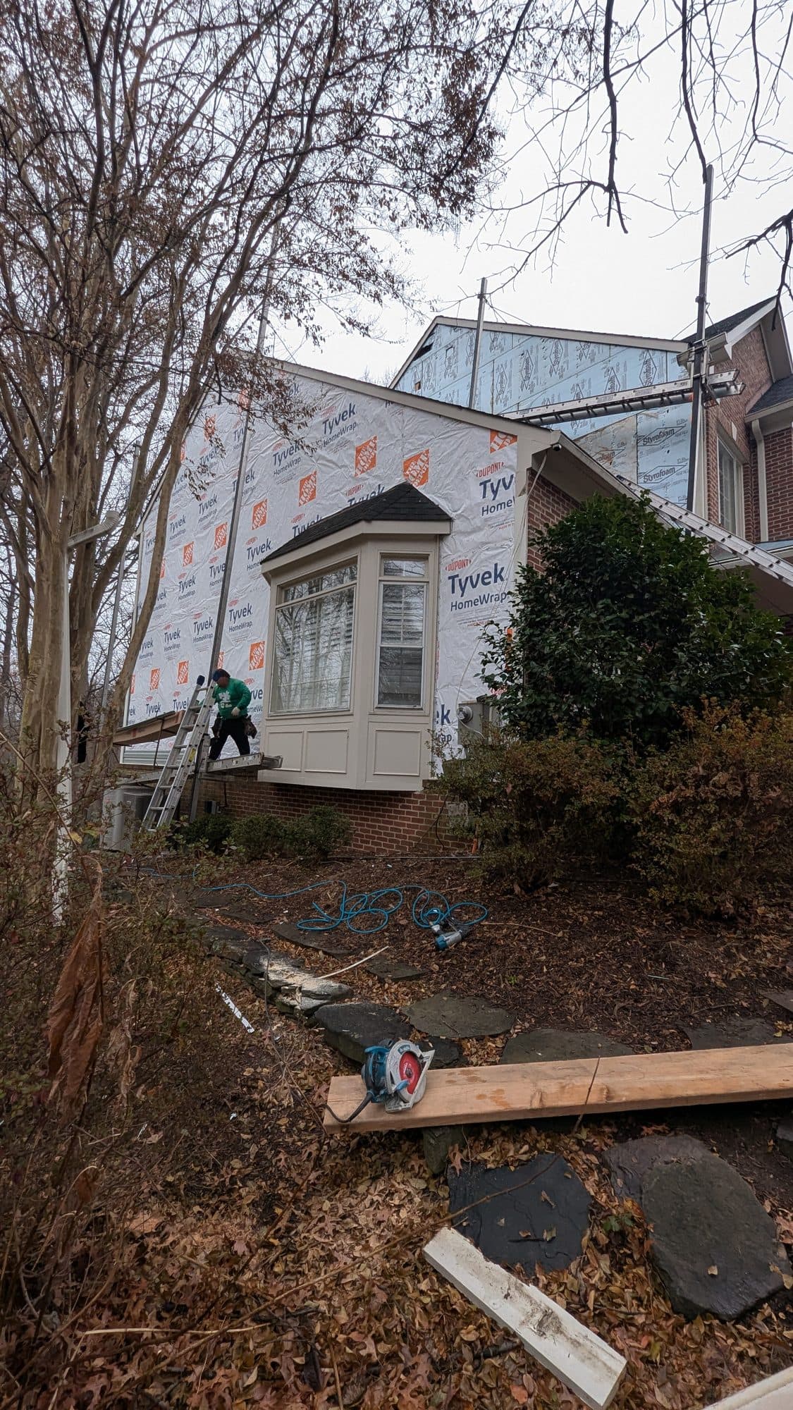 Home wrapped in house wrap with a finished bay window below, ready for new siding