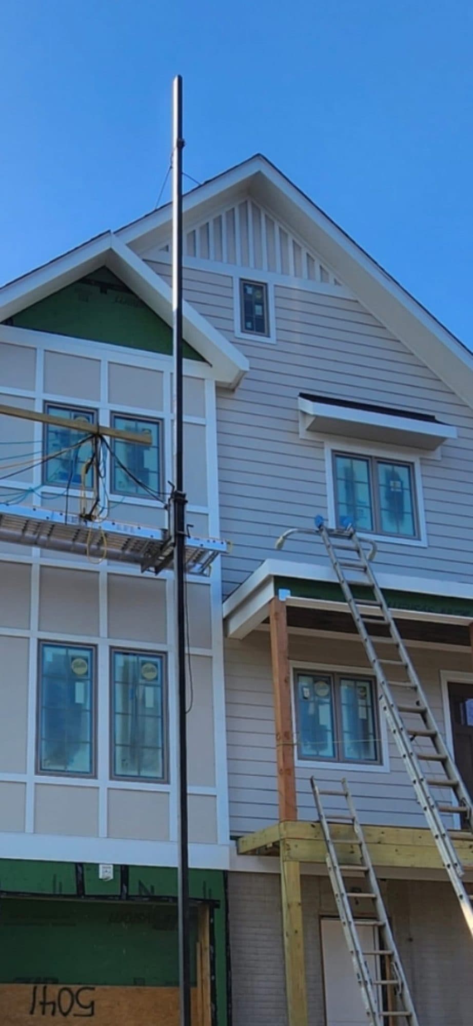 Home with tan lap siding and board-and-batten trim, scaffolding and ladders still in place